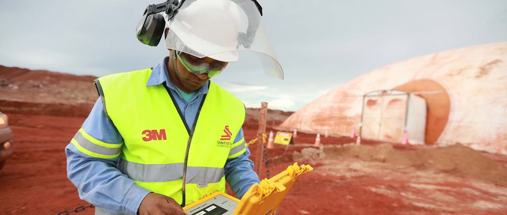 worker in hard hat and yellow vest on field of red bauxite