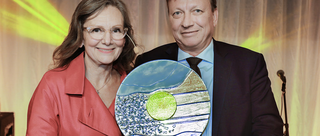 A woman and a man smiling while holding an award in recycled glass.