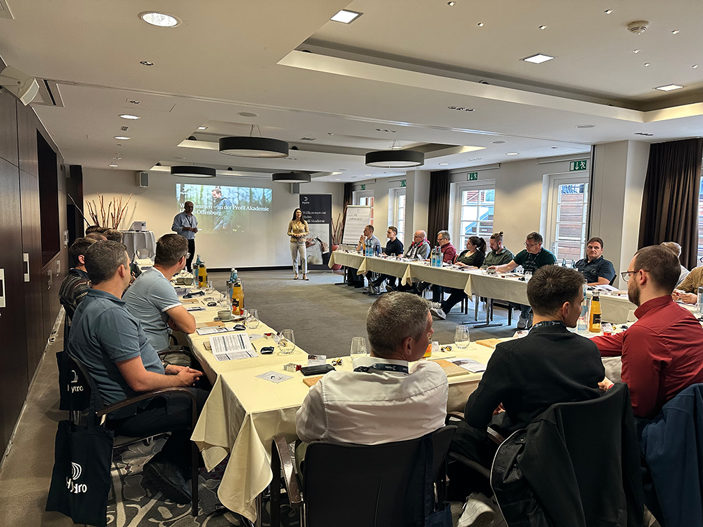a group of people sitting around a table with a person standing in front of a screen