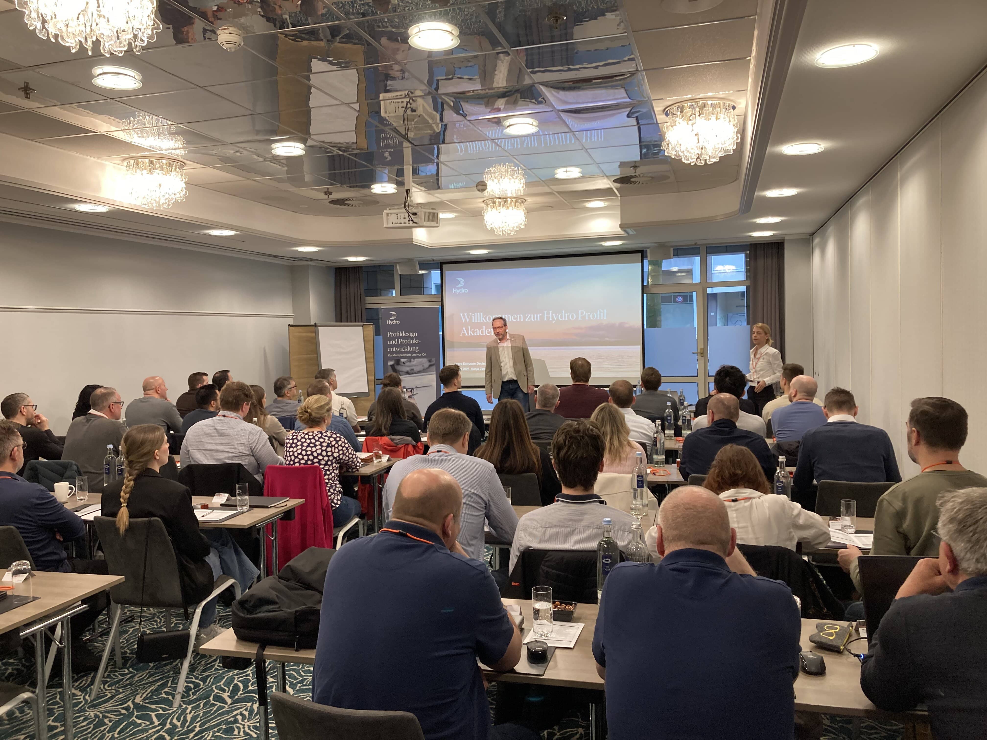 a group of people sitting in a room with a person standing in front of a projector screen