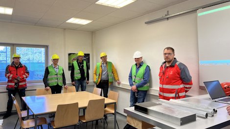 a group of men in safety vests standing in a room with tables and chairs