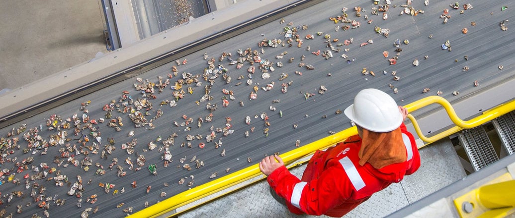 Worker observing conveyor belt with cans destined for recycling
