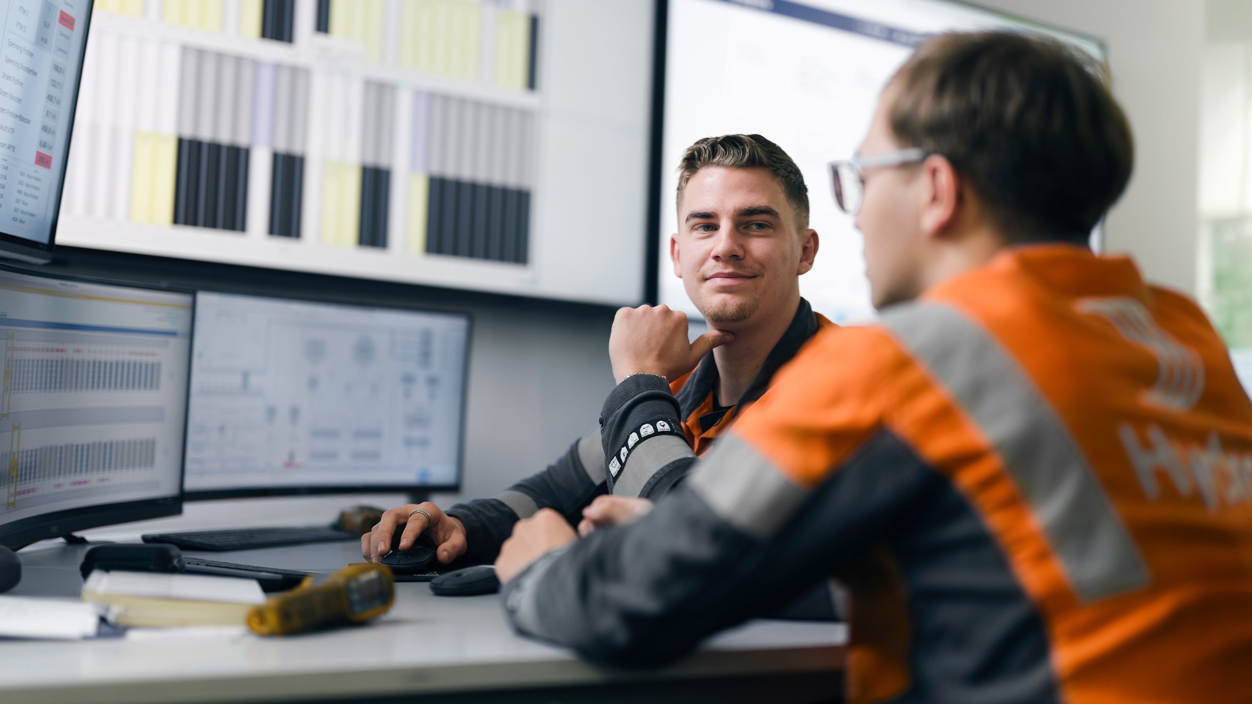 a person sitting at a desk with another man looking at him