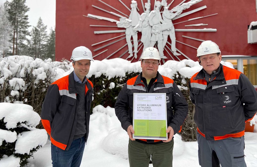 a group of men wearing hard hats and holding a certificate in front of a red building