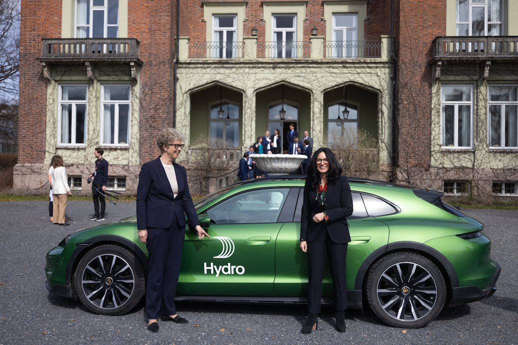 two women standing next to a green car in front of a building