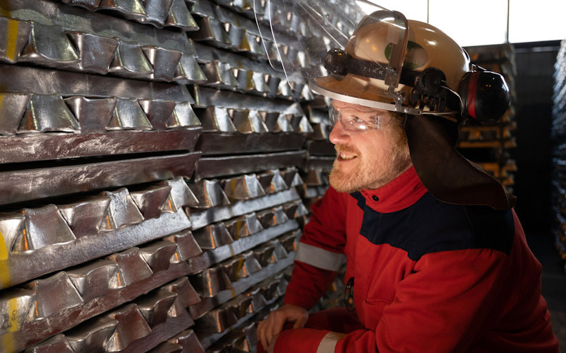 a man wearing a hard hat next to a stack of aluminium billets