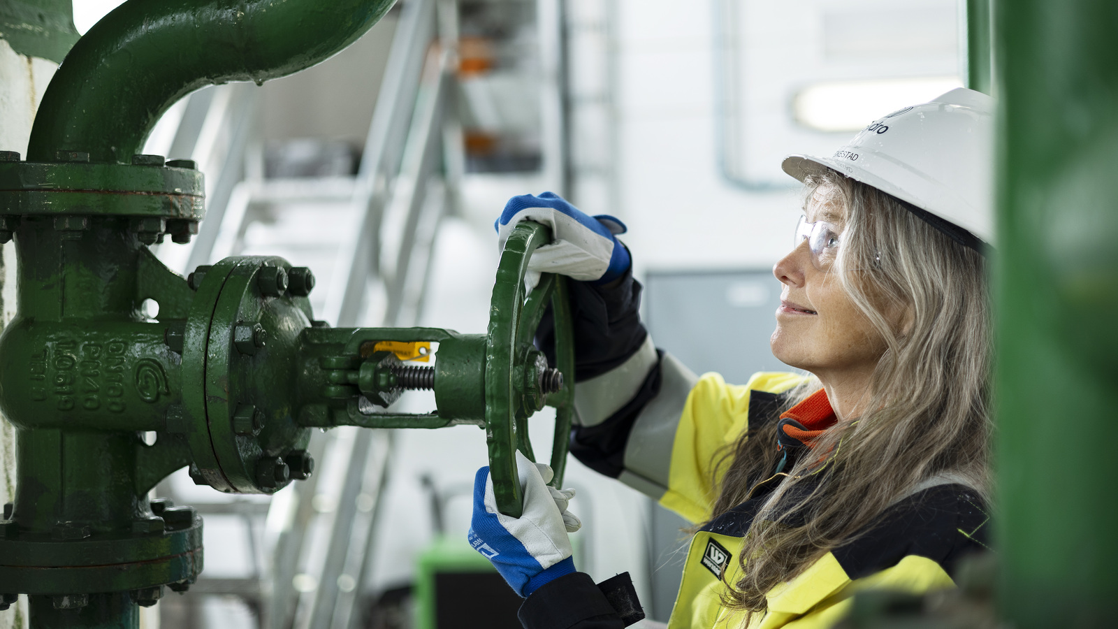 a person wearing a hard hat and gloves working on a green machine