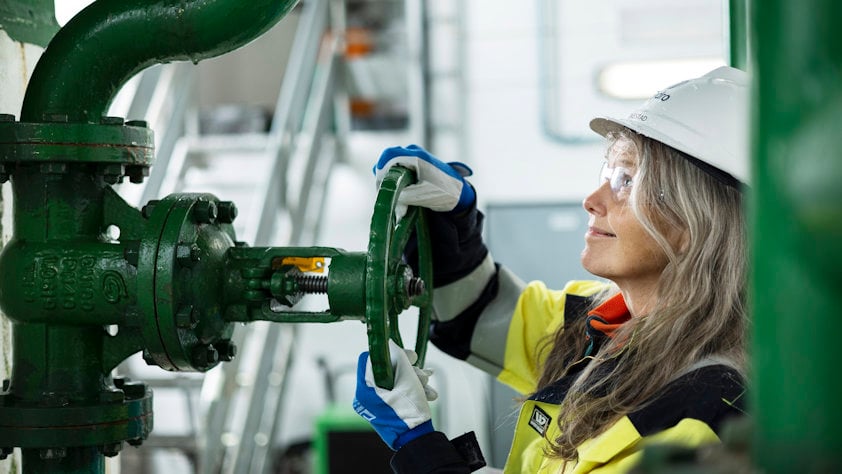 a person wearing a hard hat and gloves working on a green machine