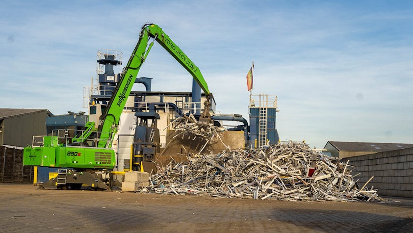 a green machine in front of a pile of scrap metal