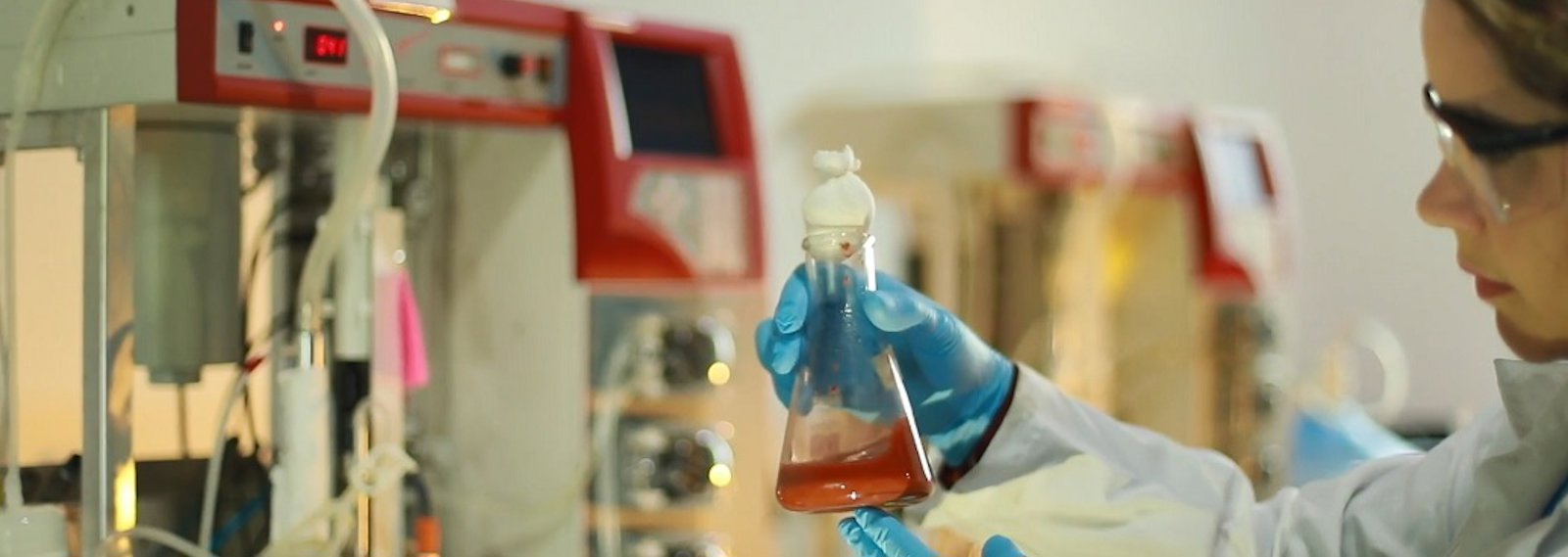 Química observando tubo de ensaio no laboratório.