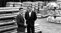 a couple of men standing in front of stacks of wood