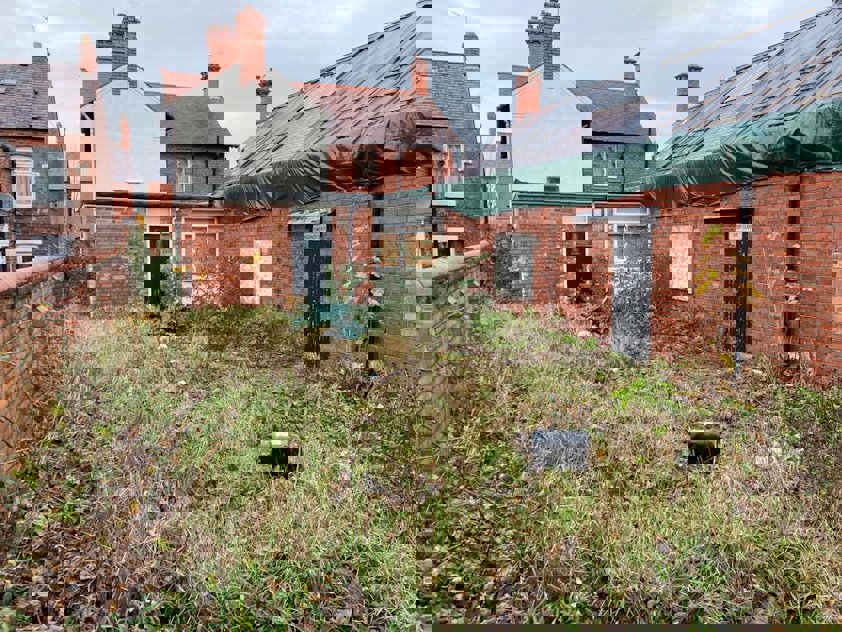 a yard with a fence and a brick building with a green roof