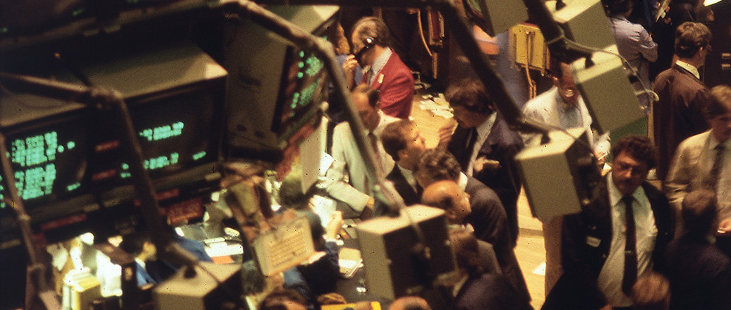 Men at the trading floor of New York Stock Exchange 1986, surrounded by screens.