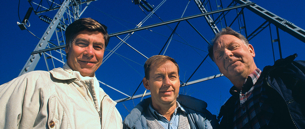 three men in front of a power mast