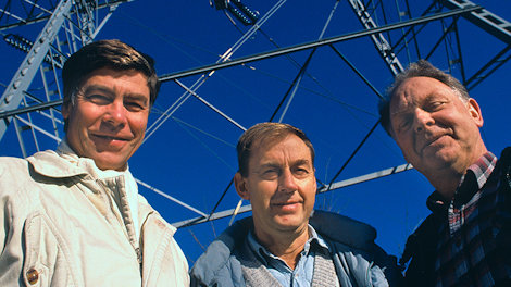 three men in front of a power mast