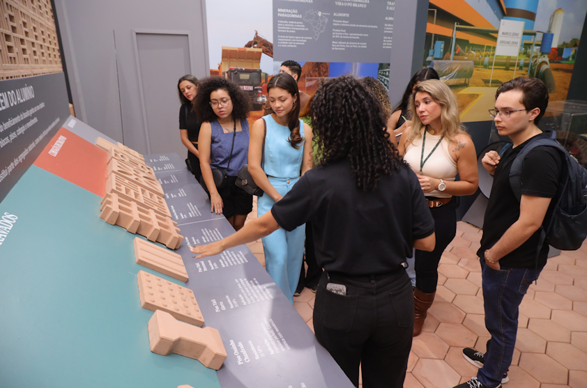a group of people standing around a table with a model of a house
