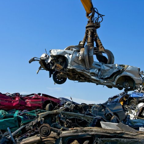 Large crane holding wrecked car over heap of scrap metal