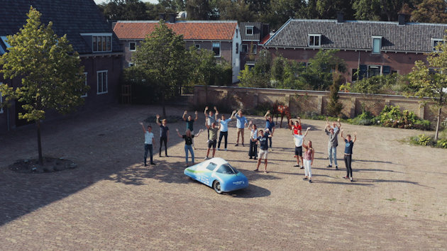 a group of people standing around a blue car