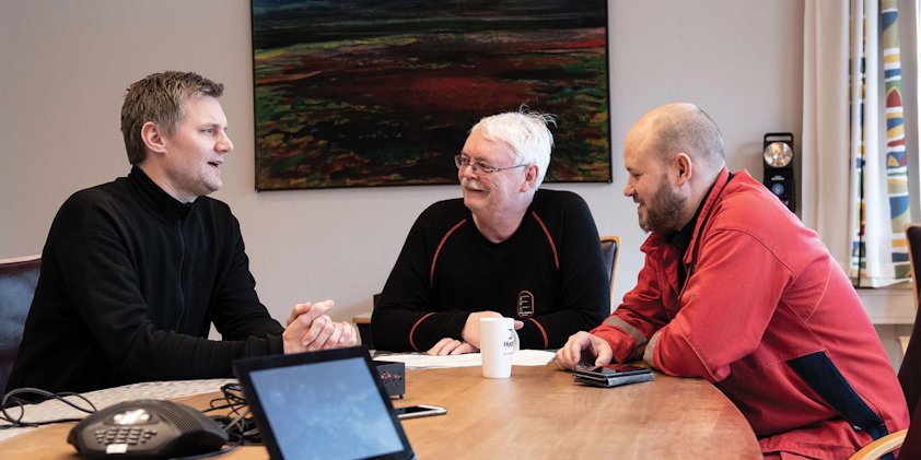 a group of men sitting at a table looking at a laptop
