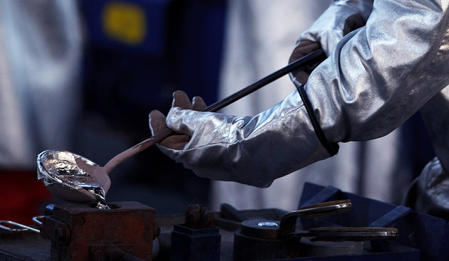 hands in protective gear pouring liquid metal into a mold