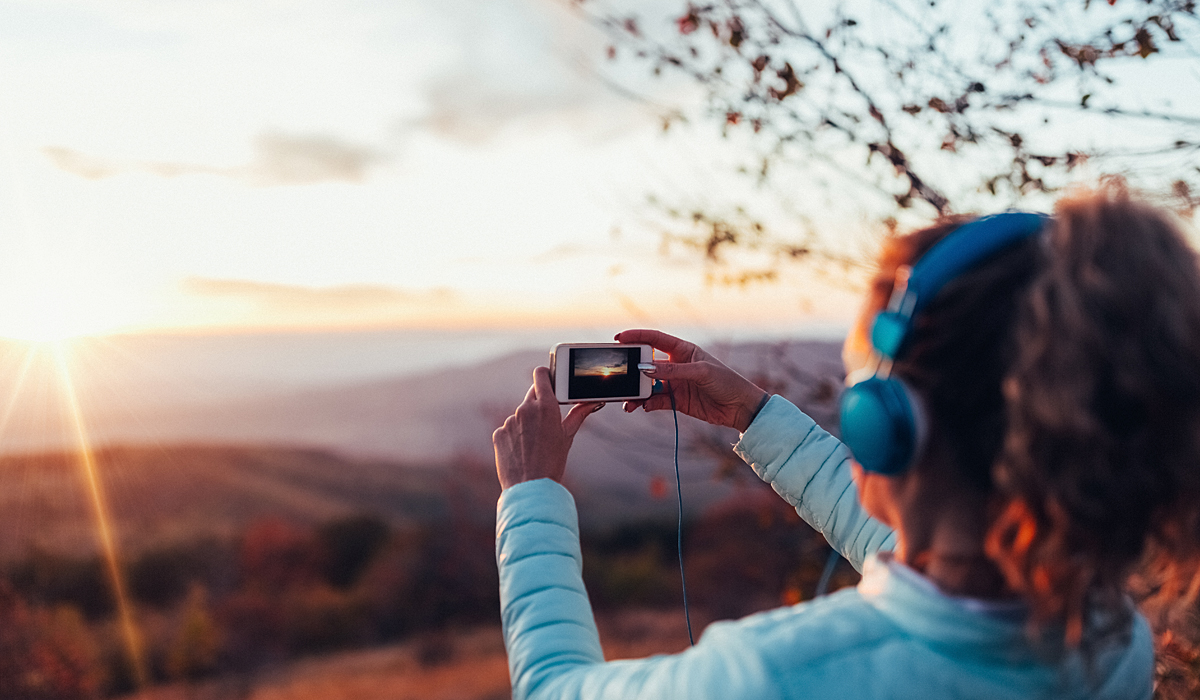 girl taking photo of sunset with smartphone