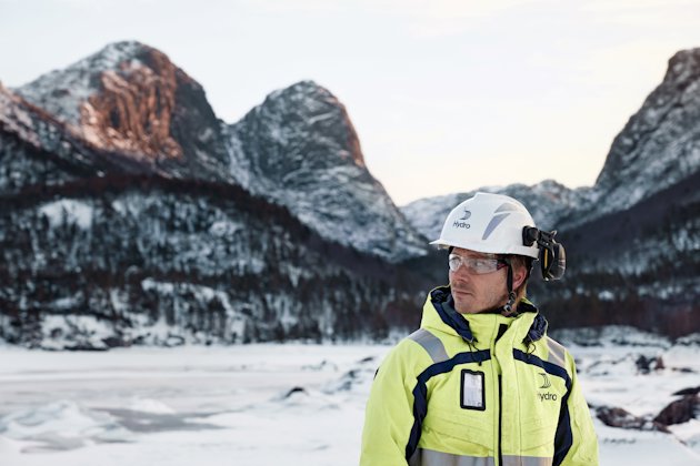 a person wearing a yellow jacket and white helmet standing in front of a snowy mountain