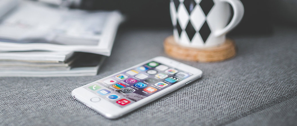 a white smart phone, magazines and a coffee mug